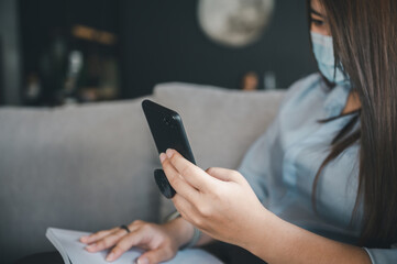 Asian woman wearing a mask uses a smartphone in a coffee shop.