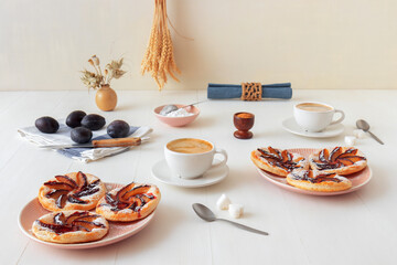 Small plum tarts on plate with cinnamon and icing sugar on white wooden table, delicious puff pastry dessert.