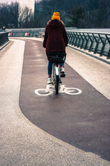 Girl wearing a bright orange hat rides a bicycle on a cycle track in the cold autumn morning, urban infrastructure