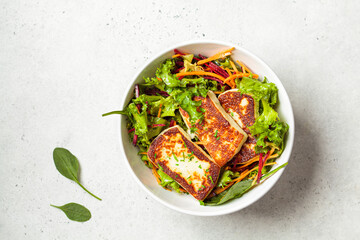 Green salad with grilled halloumi cheese, beet and carrot in a white bowl, top view. Cypriot or...