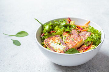 Green salad with grilled halloumi cheese, beet and carrot in a white bowl. Cypriot or Greek food concept.