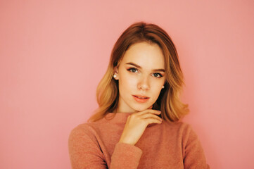 Obraz premium Close photo of a beautiful young woman in a sweater posing on a pink background, seductively looking at the camera. Cute lady isolated on pink.