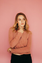 Attractive lady in a pink sweater posing for the camera on a pink background, looking away with a serious face. Vertical.