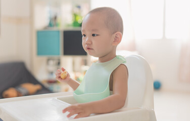 Fototapeta premium A one-and-a-half-year-old boy eats in a dining chair