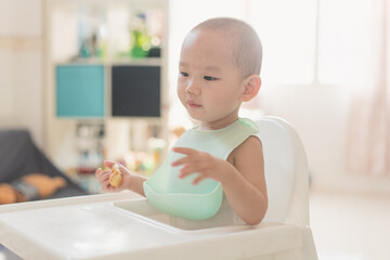 A one-and-a-half-year-old boy eats in a dining chair