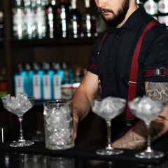 Bartender making refreshing coctail on a bar background. Dark moody style. Ice in the glass. Fosuc on model