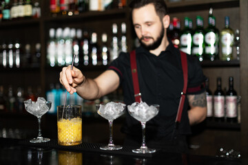 Bartender making refreshing coctail on a bar background. Dark moody style. Ice in the glass. Fosuc on hand
