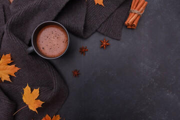 Black coffee cup, yellow maple leaves, spices, grey scarf on dark grey background. Copy space, top view. Autumn background, fall season, thanksgiving, coffee shop menu concept.