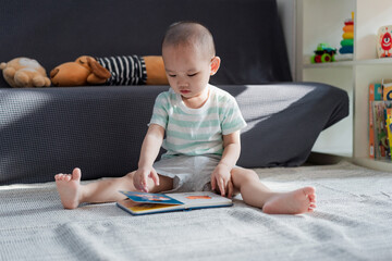 A little boy sitting on the carpet reading an early childhood picture book