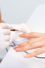 Close up of the process of applying acrylic powder on the nails of a young woman in a beauty salon