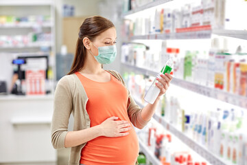 pregnancy, medicine and health concept - pregnant woman wearing protective medical mask for protection from virus disease and choosing anti stretch marks lotion at pharmacy