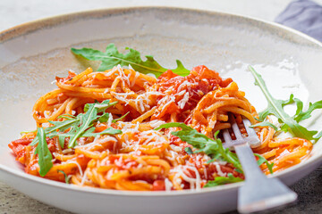 Pasta with tomato sauce, cheese and arugula in white bowl. Traditional Italian cuisine concept.