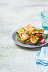 Fried halloumi sandwich with arugula and tomatoes on gray plate. Toast with grilled cheese and tomatoes.