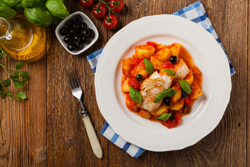Traditionally prepared cod in Spanish. Served in tomato sauce with boiled potatoes, olivki and basil. Top view.