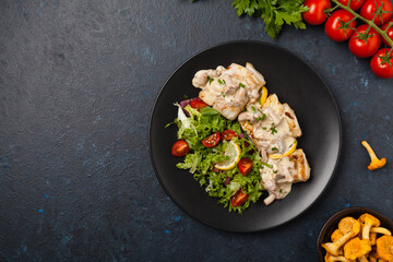 Fried cod served with mushroom sauce and salads. Portion on a black plate. Dark background.