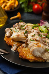 Fried cod, served on potato pancakes with mushrooms sauce and salads. Portion on a black plate. Dark background.