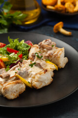 Fried cod served with mushroom sauce and salads. Portion on a black plate. Dark background.