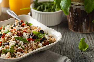 Trendy lunch with red rice, a mix of groats and vegetables. Front view. Served in white bowl on grey wooden background.