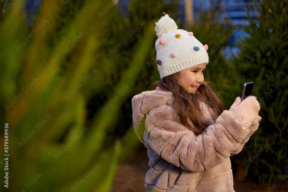 Sticker winter holidays, children and people concept -happy smiling little girl with smartphone at christmas