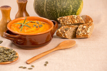 Pumpkin and carrot soup in clay bowls, a jug of pumpkin seeds and freshly baked porridge bread. Traditional autumn and winter dishes, warm and spicy