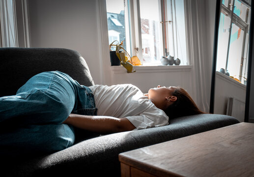 Mujer joven acostada en un sof&aacute; durmiendo en periodo de corona virus - Quedarse en casa en tiempos de COVID - Young woman lying on a sofa sleeping during the day - Staying home in times of COVID