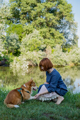 Young woman walk in the park near river with cute corgi dog