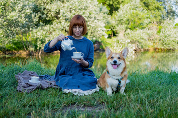 Obraz premium Young woman in retro dress with funny corgi dog on the picnic, female with cute dog drink english tea in the park