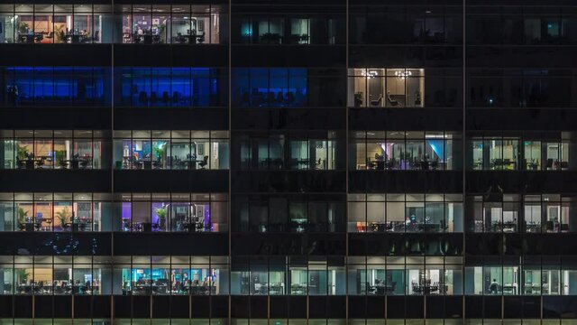 Modern office building with big windows at night timelapse close up view, in windows glowing light shines and some people inside, Singapore. Tilt down