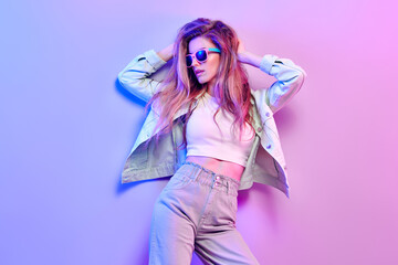 Fashionable hipster woman in Trendy outfit, stylish hair, makeup on pink purple neon light. Blonde...