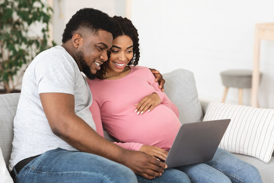 Happy african american expecting family using laptop at living room