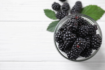 Fresh ripe blackberries in glass jar on white wooden table, closeup. Space for text