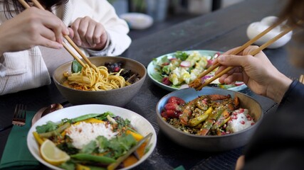 Lunch break at oriental cuisine restaurant. Meals served in colorful bowls on black wooden table. 