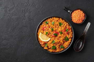 Red lentils dal in black bowl on dark slate table top. Lentils tomato dhal is indian cuisine dish with lemon and ciliantro. Indian food. Asian vegetarian meal Top view. Copy space