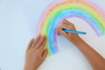 Little child drawing rainbow on white background, top view. Stay at home concept