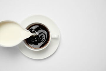 Pouring milk into cup of coffee on white background, top view