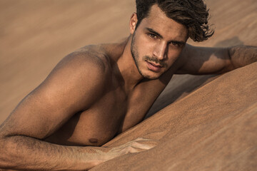 Portrait of sexy handsome shirtless male model on the desert sand dunes. 