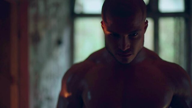 An athletic man with a naked torso walks through a destroyed building medium shot