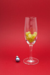 Twelve grapes in a glass for sparkling wine cava. Selective focus, red background, copy space. Spanish traditional to eat twelve 12 berries for good luck at midnigth. Christmas New Year composition