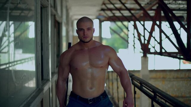 Athletic man walks through an abandoned building in shorts and holding a hammer