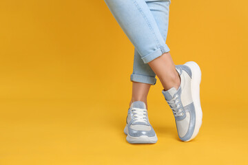 Woman wearing stylish sneakers on yellow background, closeup. Space for text
