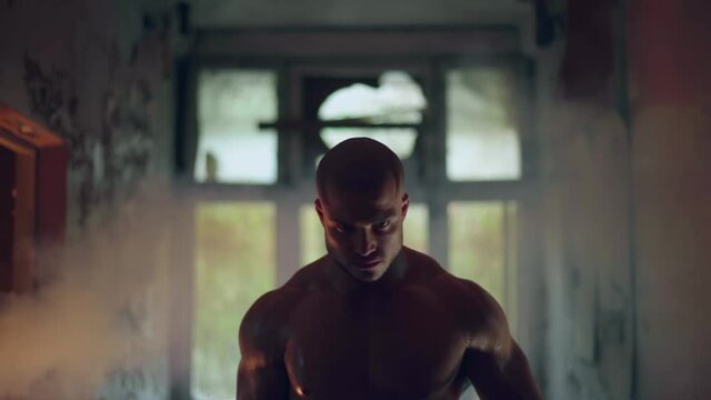 An athletic man with a naked torso walks through a destroyed building big clous up