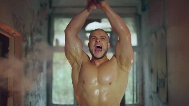 An athletic man with a naked torso walks through a destroyed building big clous up