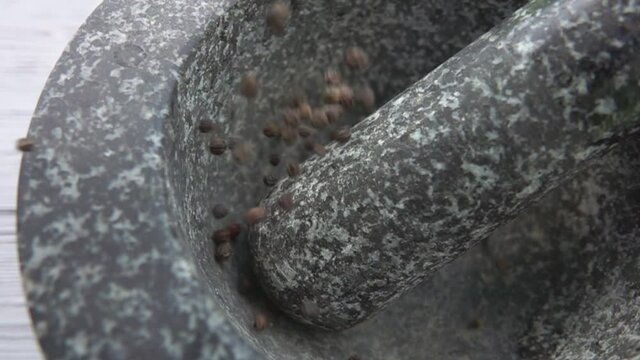 Close-up of black peppercorns falling into the grey stone mortar in slow motion