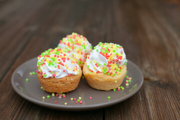 Three cupcakes with colored sprinkles on a gray ceramic plate on an old dark wood table