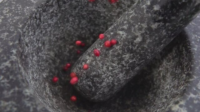 Red peppercorns are falling into the grey stone mortar in slow motion