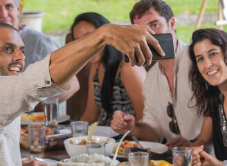 Group of diverse multiethnic friends making selfie photo in outdoor restaurant or home. Happy men and women smiling to the camera while having meal together