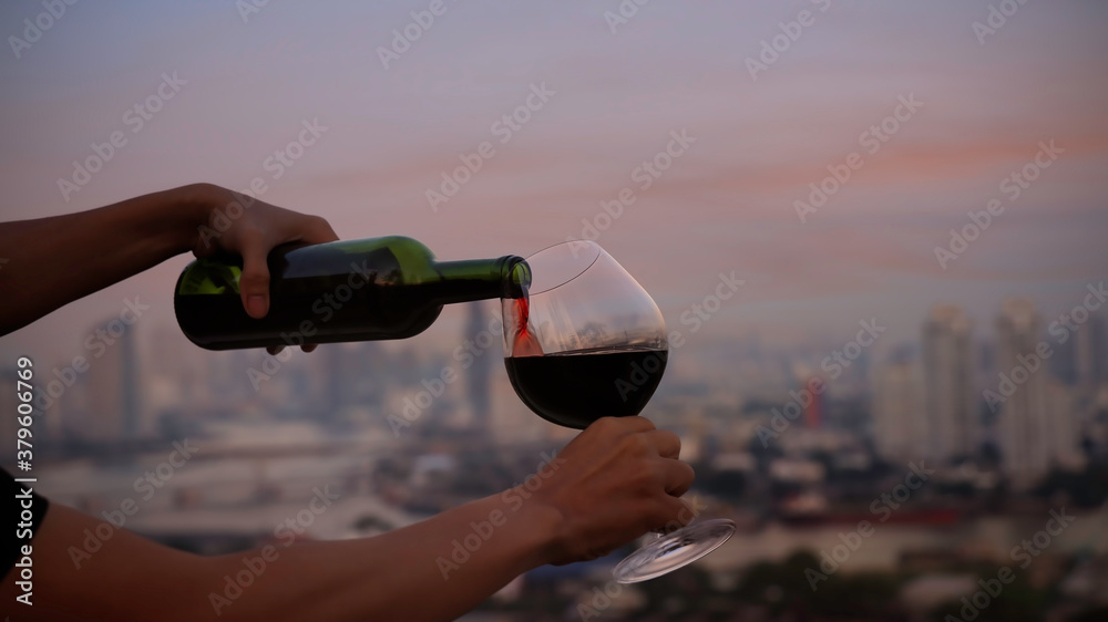 Wall mural waiter pouring red wine in a glass on the rooftop with city and sunset sky scene