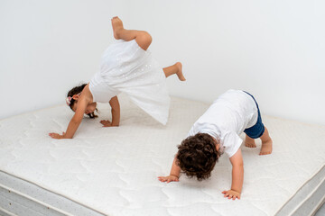 Two crazy cheerful cheery positive preschool siblings having fun, jump on the mattress in a home...