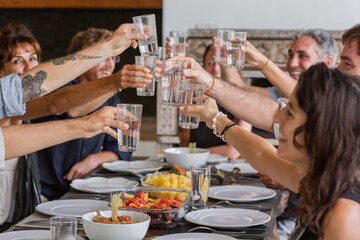 Diverse group of multiethnic friends toasting with glasses and enjoying meal in outdoor cafe or home. Leisure, food and drinks, people and holidays concept