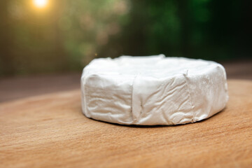 a circle of soft brie cheese with white mold from cow's milk on a wooden board on a green bokeh background. close-up. place for text